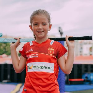 niña con el palo de hockey posado en los hombros lleva camiseta femenina de la selección española de hockey hierba