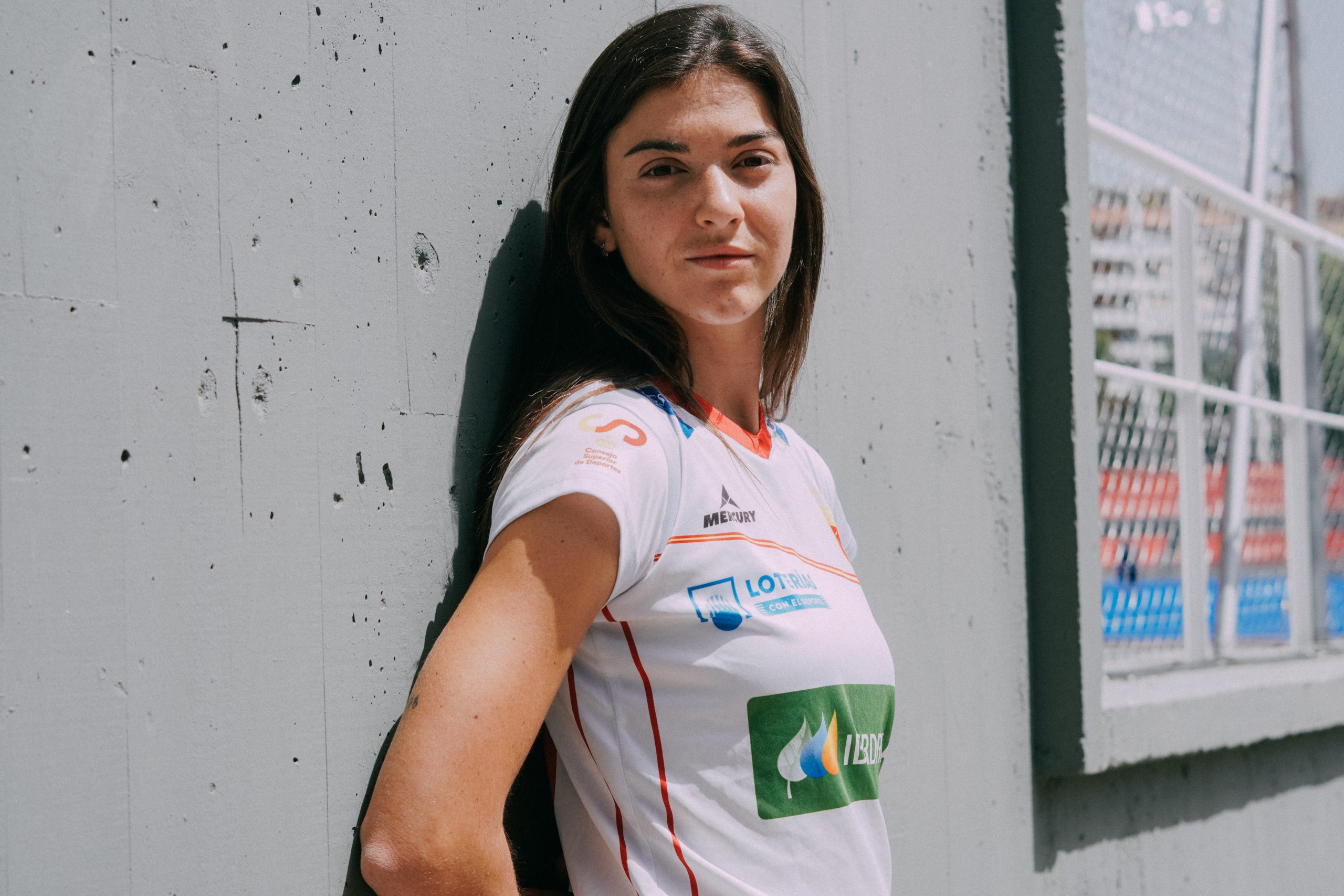 Chica apoyada en la pared con la camiseta blanca de las redsticks de hockey hierba