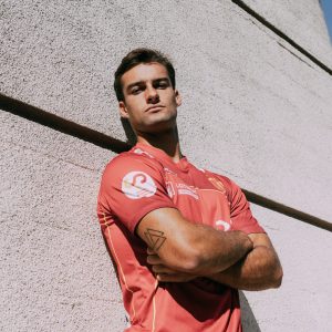 chico apoyado en la pared mirando desafiante a cámara con los brazos cruzados y la primera equipación de la selección española de hockey hierba