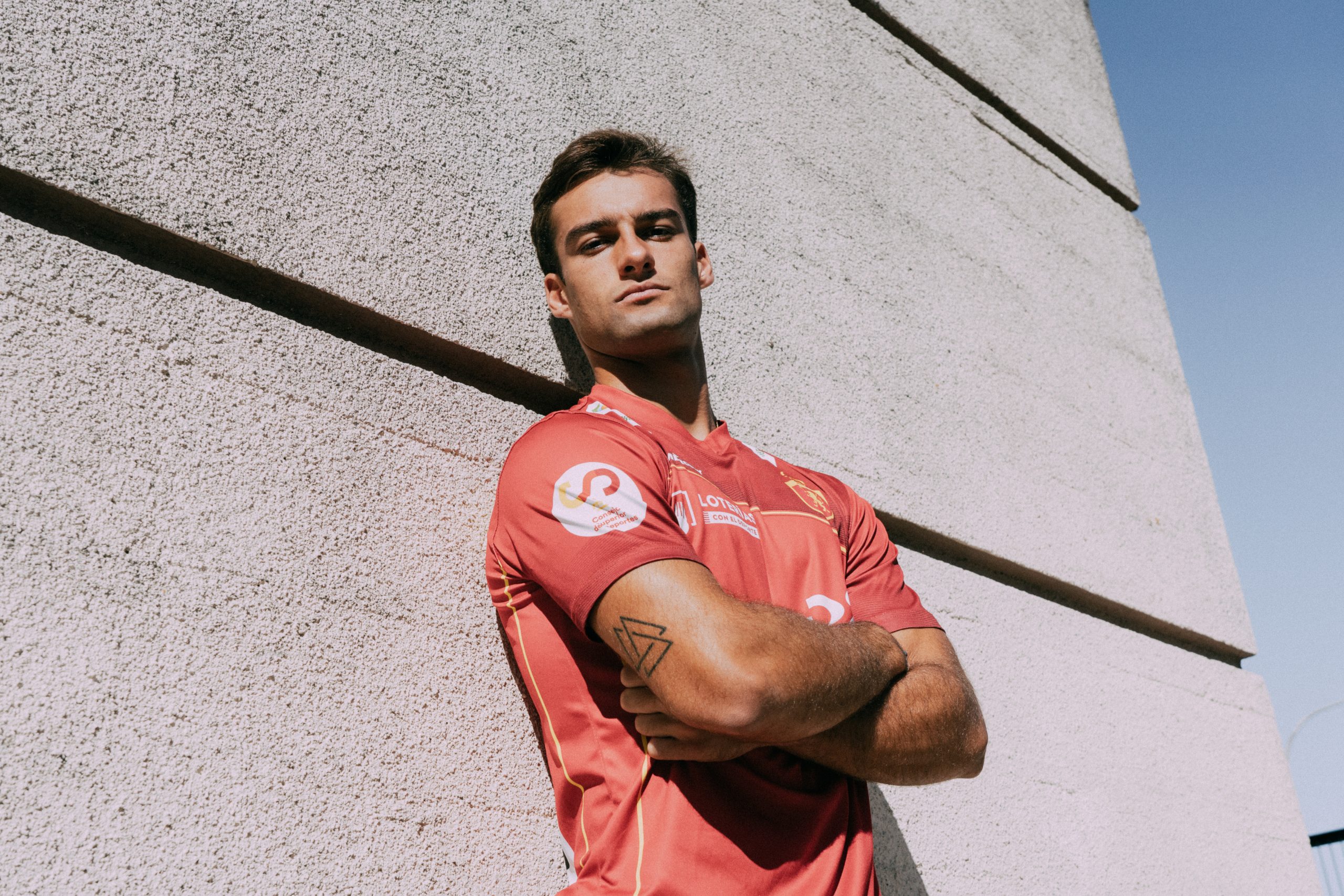 chico apoyado en la pared mirando desafiante a cámara con los brazos cruzados y la primera equipación de la selección española de hockey hierba