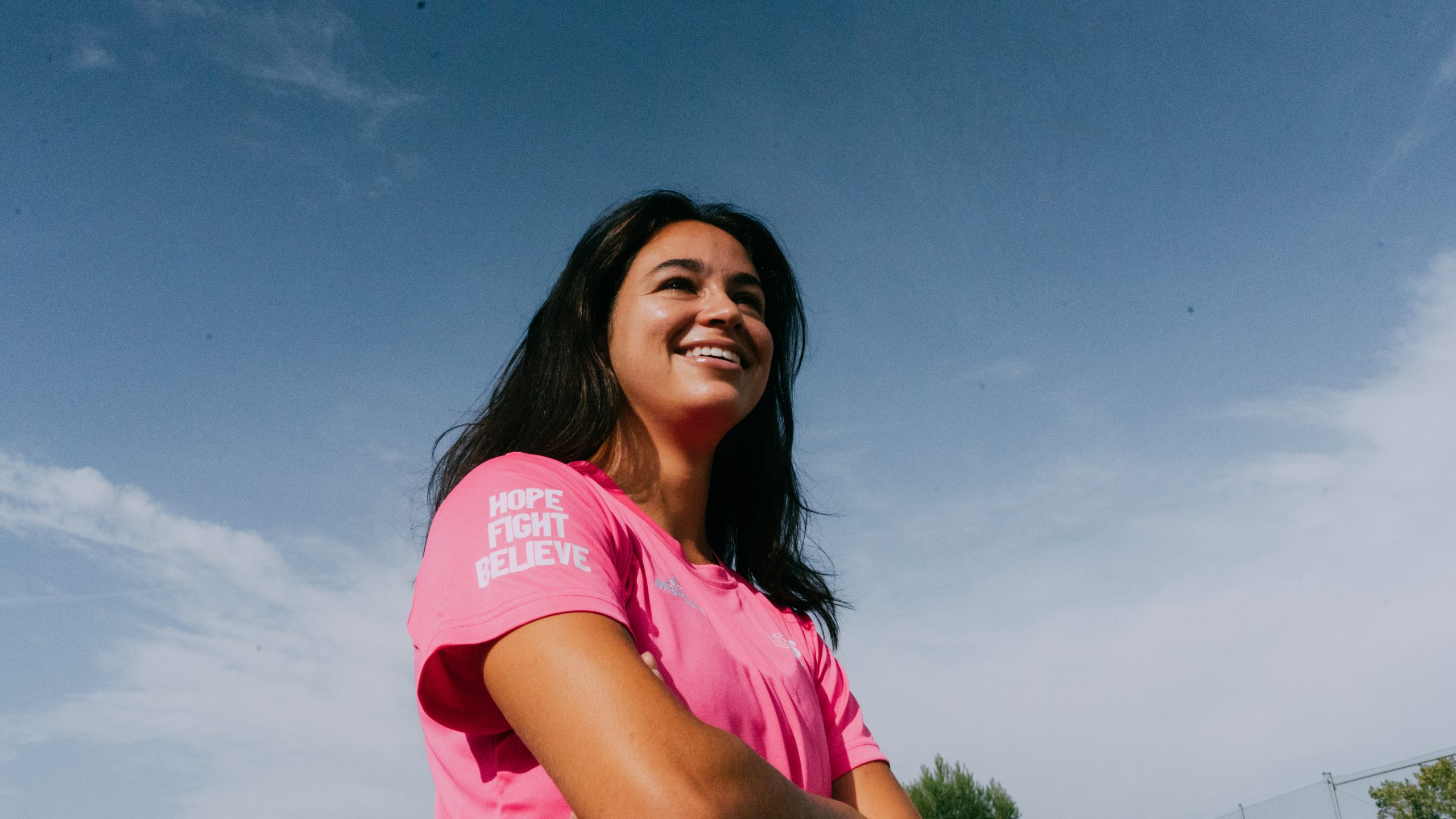 jugadora de la selección de hockey mirando a lo lejos con la camiseta solidaria redsticks en favor de la lucha contra el cancer de mama y con las palabras HOPE FIGHT BELIEVE en la manga derecha