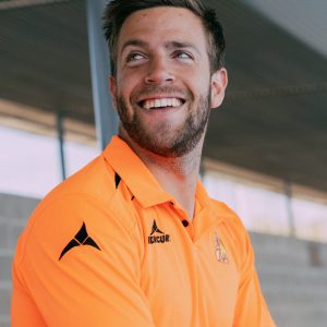 Hombre sonríe con el polo de árbitraje naranja fosforito de hockey hierba